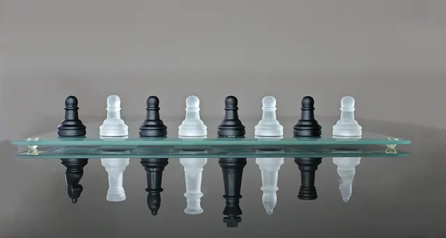 Image of chess pawns on a glass table, the reflection of each is the corresponding main piece